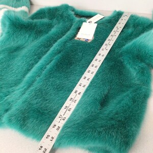 Op de afbeelding: Een teal-kleurige imitatiebontjas met een ronde hals en lange mouwen. Een liniaal ligt over de jas en meet ongeveer 61 cm. Een bijpassende teal-kleurige hoed met witte strepen is zichtbaar. Een label is bevestigd.