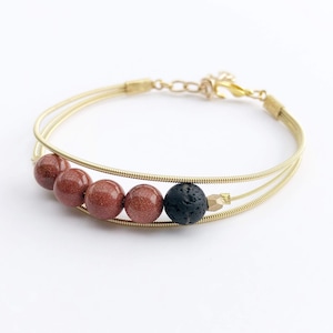 Może przedstawiać: Bransoletka z złotych strun gitarowych z czerwonymi i czarnymi koralikami. Bransoletka ma zapięcie.