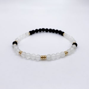 May include: A white and black beaded bracelet with gold accents. The bracelet is made with small, round beads and has a simple, elegant design.