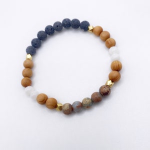 May include: A beaded bracelet with black lava rock, brown wood, white and brown jasper, and gold accents.
