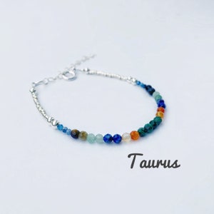May include: A silver bracelet with a variety of colorful beads, including blue, green, orange, and brown. The bracelet is labeled "Taurus".