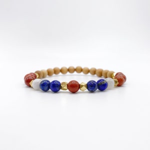 May include: A beaded bracelet with red, blue, white, and gold beads. The bracelet is made with wooden beads and gemstone beads.