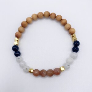 May include: A bracelet with wooden, white, brown, and black beads. The beads are separated by gold spacers.