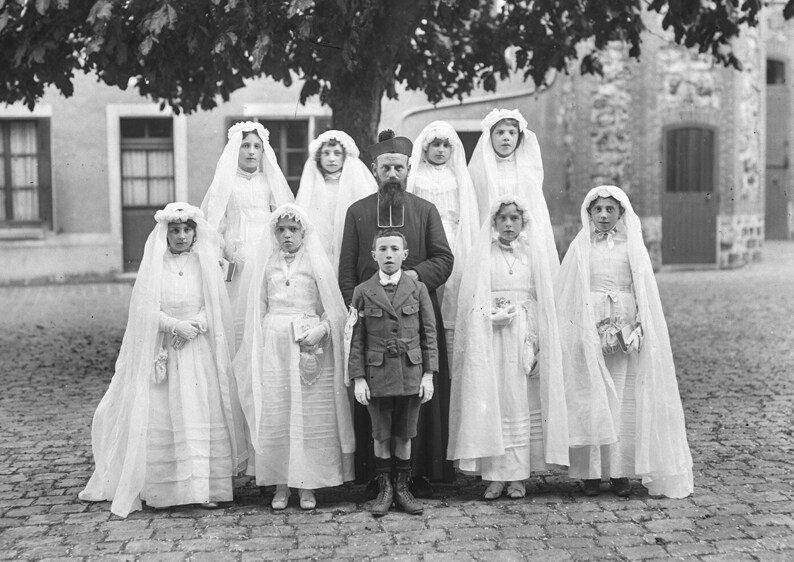 K&ouml;nnte beinhalten: Eine Gruppe von Kindern, alle in Wei&szlig; mit Schleiern gekleidet, stehen vor einem Mann in einer schwarzen Robe. Sie l&auml;cheln alle und schauen in die Kamera. Die Kinder halten kleine wei&szlig;e B&uuml;cher in ihren H&auml;nden.