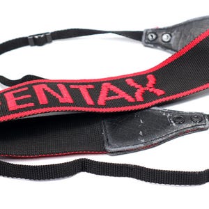 May include: Black and red camera strap with the word "PENTAX" embroidered in red.
