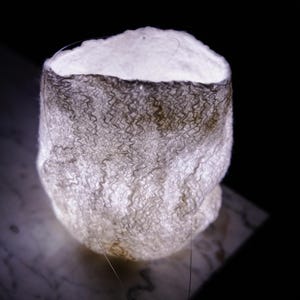 Peut inclure: Un bol décoratif blanc cassé et gris texturé et lumineux. Le bol a une base arrondie et un sommet cylindrique. L'intérieur est blanc vif et l'extérieur a une texture ondulée et à motifs. Le fond est noir.