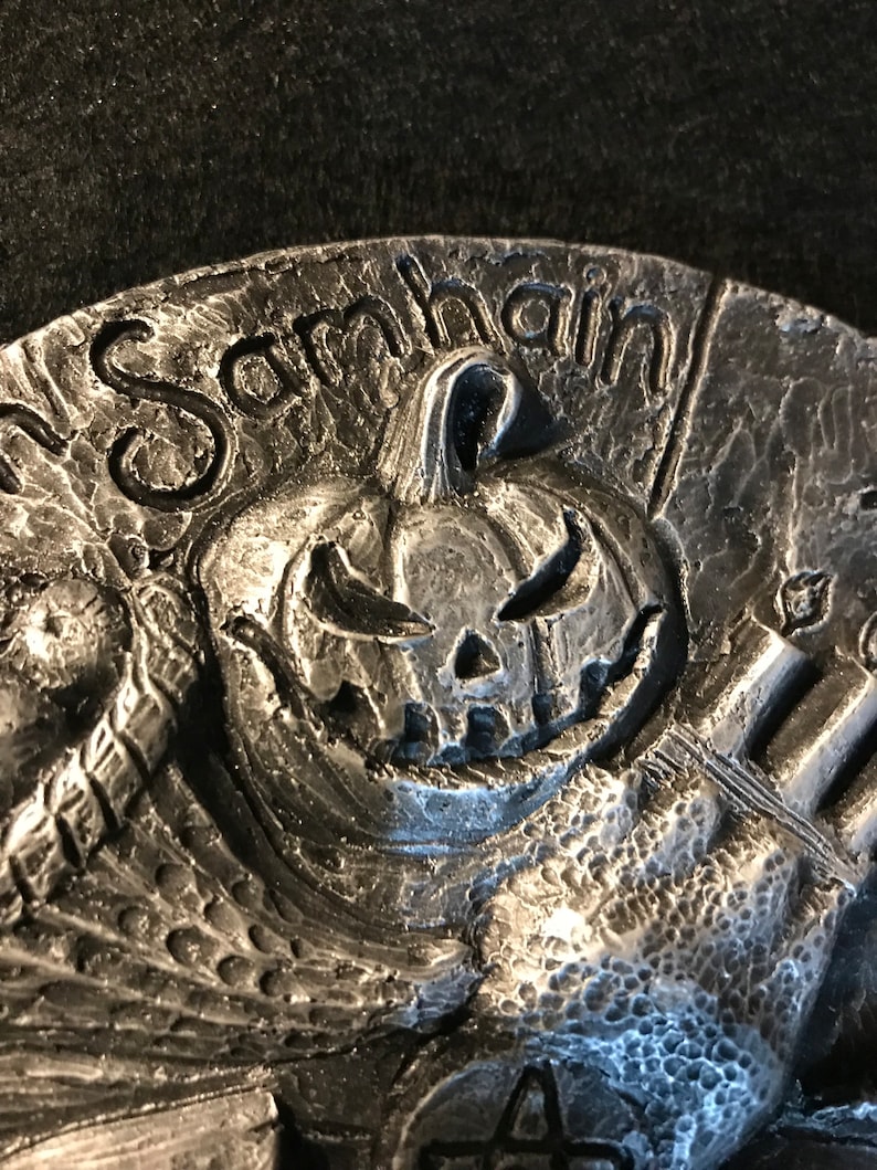 May include: A silver-toned metal ornament with a carved pumpkin face and the word "Samhain" inscribed around the top.