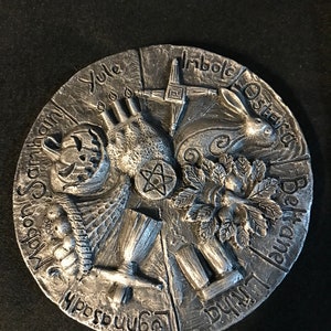 May include: A silver circular wheel with eight sections, each representing a different Celtic holiday. The wheel is decorated with symbols and text, including the names of the holidays: Yule, Imbolc, Ostara, Beltane, Litha, Lammas, Mabon, and Samhain.