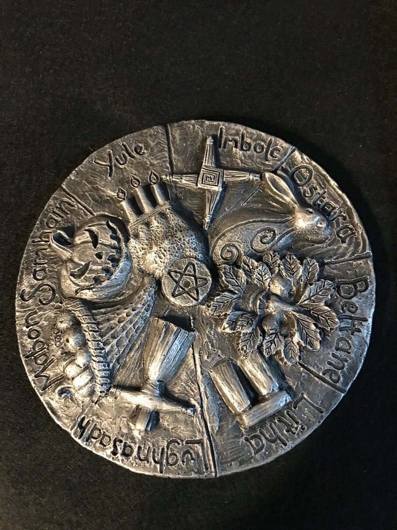 May include: A silver circular wheel with eight sections, each representing a different Celtic holiday. The wheel is decorated with symbols and text, including the names of the holidays: Yule, Imbolc, Ostara, Beltane, Litha, Lammas, Mabon, and Samhain.