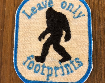 May include: A white patch with a blue border features a black silhouette of a Bigfoot walking with the text "Leave only footprints" in blue.