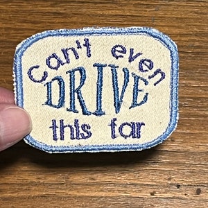 May include: Embroidered patch with the words "Can't even DRIVE this far" in blue script on a cream-colored background. The patch has a light blue border and a rectangular shape with rounded corners.