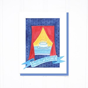 May include: A birthday card with a blue background and white polka dots. A red curtain is pulled back to reveal a white cake with lit candles. The text on the card reads "What light through yonder window breaks!"