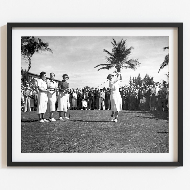 Pode incluir: Uma fotografia a preto e branco de quatro mulheres a jogar golfe. A mulher em primeiro plano est&aacute; a balan&ccedil;ar o seu taco, enquanto as outras tr&ecirc;s mulheres observam. H&aacute; muitas pessoas no fundo a assistir ao jogo.