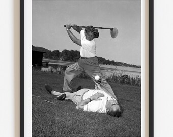 Puede incluir: Una fotografía en blanco y negro de dos hombres en un campo de golf. Un hombre está balanceando un palo de golf hacia el otro hombre que está tirado en el suelo.