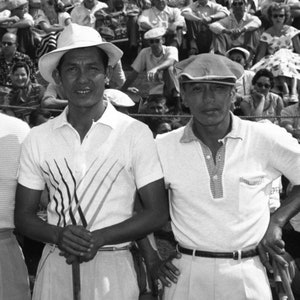 Puede incluir: Dos hombres con camisas blancas y sombreros se paran juntos. El hombre de la izquierda lleva un sombrero blanco de ala ancha y una camisa blanca con un dise&ntilde;o de rayas blancas y negras. El hombre de la derecha lleva una gorra plana y una camisa blanca con un dise&ntilde;o de rayas azules y blancas. Ambos est&aacute;n sonriendo.