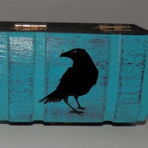 May include: A small wooden box painted turquoise blue with a black silhouette of a crow on the front.