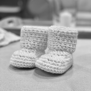 May include: A pair of white crocheted baby booties with a fold-over cuff.