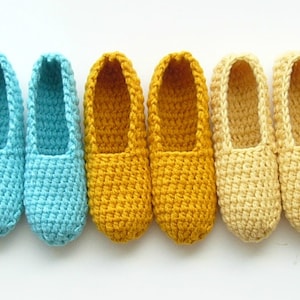 Könnte beinhalten: Vier Paar gehäkelte Hausschuhe in verschiedenen Farben: Blau, Gelb und Creme. Die Hausschuhe sind mit einem strukturierten Stich gearbeitet und haben eine einfache, abgerundete Spitze.