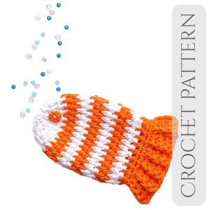 May include: A crocheted fish toy in orange and white, with a small orange button eye. The fish has a textured tail and a striped body. The words "CROCHET PATTERN" are printed vertically on the right side of the image. Small blue and white beads are scattered above the fish.