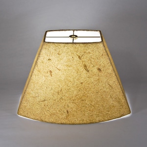 May include: A beige lampshade with a square top and a curved bottom. The lampshade is made of a textured material that resembles paper.