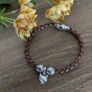 May include: A brown leather bracelet with a silver fox charm and two silver bead accents. The bracelet has a magnetic clasp.