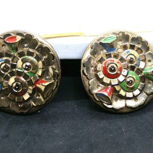 May include: A pair of gold-tone earrings with a circular design. The earrings feature a multi-colored enamel design with red, green, blue, and yellow accents.