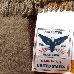 May include: Close-up of a woven textile with a tag. The tag reads "PENDLETON" with an eagle emblem and "HIGHEST QUALITY" and "MADE IN THE UNITED STATES". The textile has a brown, tan, and orange colour scheme.