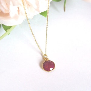 May include: A gold chain necklace with a round, faceted ruby pendant.