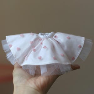 Op de afbeelding: Een witte tule rok met roze hartvormige versieringen. De rok heeft een gerimpelde zoom en is perfect voor een pop of een klein kind.
