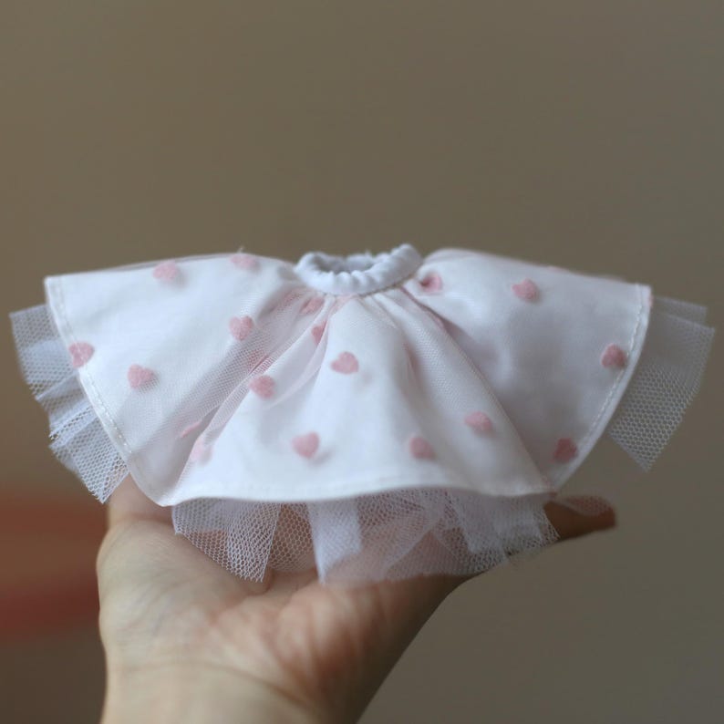 Op de afbeelding: Een witte tule rok met roze hartvormige versieringen. De rok heeft een gerimpelde zoom en is perfect voor een pop of een klein kind.