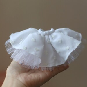 Op de afbeelding: Een witte tule rok met een witte katoenen overlay met een hartjespatroon. De rok heeft een elastische tailleband.