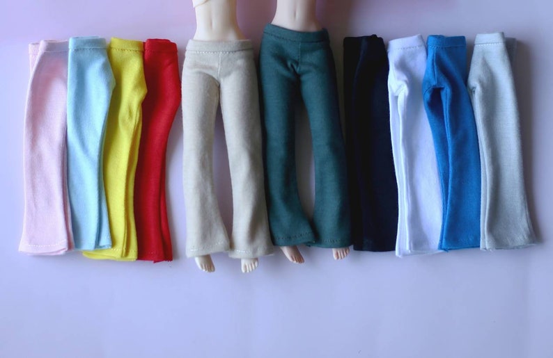 K&ouml;nnte beinhalten: Ein Set mit zehn Paaren Puppenhosen in verschiedenen Farben, darunter rosa, hellblau, gelb, rot, beige, gr&uuml;n, schwarz, wei&szlig;, blau und grau.