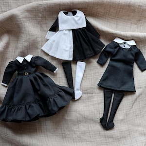 May include: Three doll dresses in black and white, with white collars and cuffs. One dress is split down the middle, with one side black and the other white. Two pairs of doll stockings are also included.