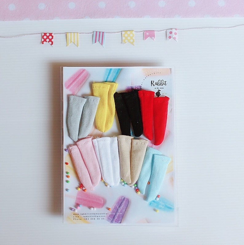 May include: A set of 10 pairs of colorful miniature socks in a clear plastic package. The socks are arranged in two rows, with the top row featuring red, black, yellow, and gray socks. The bottom row features pink, white, beige, and light blue socks. The package has a label that says "Rabbit in the moon".