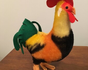 May include: A plush toy rooster with a red comb, green tail feathers, and black, orange, and yellow patterned body.