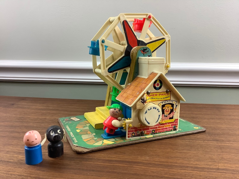 K&ouml;nnte beinhalten: Vintage Fisher-Price Little People Spielset mit einem bunten Riesenrad, einem kleinen Haus mit einem Drehknopf und zwei Little People Figuren. Das Haus hat ein Schild mit der Aufschrift "Fisher-Price Little People Ferris Wheel".