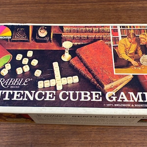 May include: A rectangular Scrabble Brand Sentence Cube Game box from 1971 by Selchow & Righter Co. The box features a graphic of white lettered cubes, a green-lined shaker, two leather-bound books, and a photo of two people playing the game.