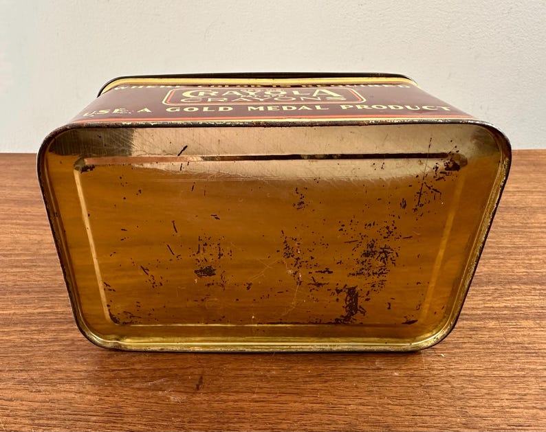 May include: A vintage Crayola crayon tin, rectangular with a trapezoidal shape, in shades of brown and gold. The top features the Crayola logo and the text "USE A GOLD MEDAL PRODUCT". The tin shows signs of age and wear.