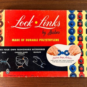 May include: A vintage box of Lock Links by Hasbro, a snap-together toy for making bracelets, belts, and hair accessories. The box features a red background with the product name and instructions for use. The box is made of durable polyethylene.