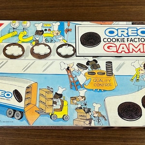 May include: Vintage Oreo Cookie Factory Game box. The box features a colorful illustration of an Oreo cookie factory with workers, trucks, and the text "OREO COOKIE FACTORY GAME". The Nabisco logo is visible in the corner.