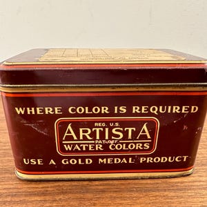 May include: A vintage rectangular Artista water colors tin. The tin is a deep maroon color with gold trim and lettering. The text on the tin reads "WHERE COLOR IS REQUIRED" and "ARTISTA WATER COLORS".