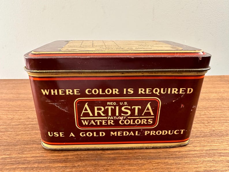 May include: A vintage rectangular Artista water colors tin. The tin is a deep maroon color with gold trim and lettering. The text on the tin reads "WHERE COLOR IS REQUIRED" and "ARTISTA WATER COLORS".
