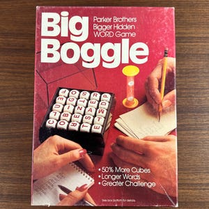 May include: A vintage Big Boggle word game box with a red background. The box features the game title in large white letters and the Parker Brothers logo. The image shows the game's components, including letter cubes, a timer, and a notepad. The text on the box reads "50% More Cubes, Longer Words, Greater Challenge."