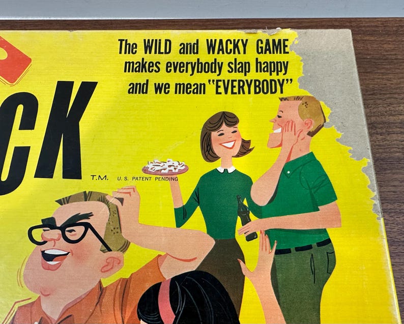 Puede incluir: Caja de juego de mesa vintage con fondo amarillo e ilustraciones de dibujos animados. El texto dice "The WILD and WACKY GAME makes everybody slap happy and we mean 'EVERYBODY'". Presenta un dise&ntilde;o retro con personajes sonrientes.