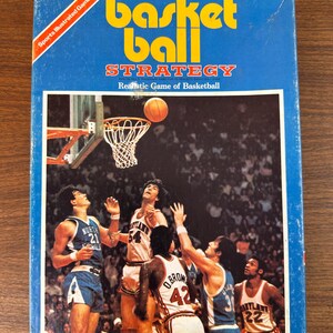 May include: A blue box with a basketball game on the front. The box has the words "Basketball Strategy" and "Realistic Game of Basketball" on it. The game is made by Avalon Hill Game Co. and is printed in the USA.