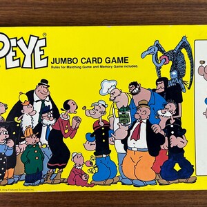 May include: A rectangular yellow Popeye Jumbo Card Game box featuring a colorful illustration of various cartoon characters from the Popeye series. The right side displays a single card with an image of Popeye and the text Actual size of card.