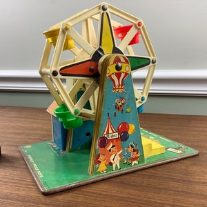 K&ouml;nnte beinhalten: Vintage Fisher-Price Little People Spielset mit einem bunten Riesenrad, einem blauen und gelben Hei&szlig;luftballon und einem gr&uuml;n-gelb gestreiften Zelt. Das Set enth&auml;lt eine gr&uuml;ne Basis mit dem Aufdruck "Fisher-Price Toys".