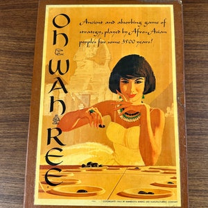 May include: A wooden game box with a colorful illustration of a woman playing a board game called "Oh Wah Ree". The box features the text "Ancient and absorbing game of strategy, played by Afro-Asian peoples for some 3500 years!" and "COPYRIGHT 1962 BY MINNESOTA MINING AND MANUFACTURING COMPANY".