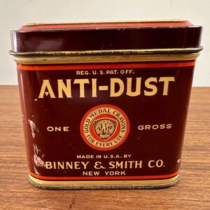 May include: A vintage rectangular tin with a maroon and gold color scheme. The text "ANTI-DUST" is prominently displayed in large, gold letters. The tin also features the text "ONE GROSS" and "GOLD MEDAL CRAYONS". The manufacturer's name, "BINNEY & SMITH CO., NEW YORK" is also visible.