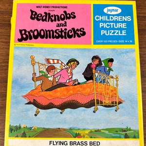 May include: A vintage children's picture puzzle featuring a scene from the Walt Disney movie Bedknobs and Broomsticks. The puzzle shows the characters riding on a flying brass bed with a pink and orange patterned mattress. The box is yellow with a pink and black title and the text "Over 100 pieces - Size 14 x 19".